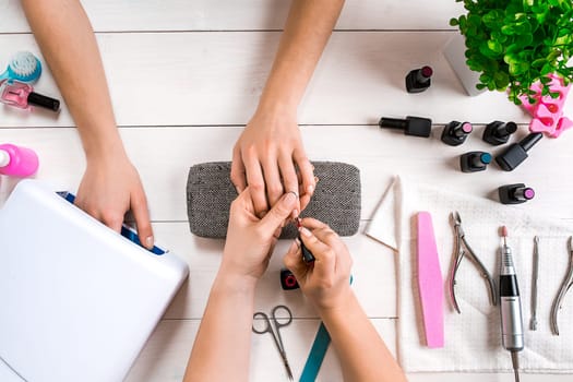 Nail care. Closeup of female hands filing nails with professional nail file in beauty nail salon. Close-up of beautician hands doing perfect manicure on woman's hands. Nail hygiene. Top view