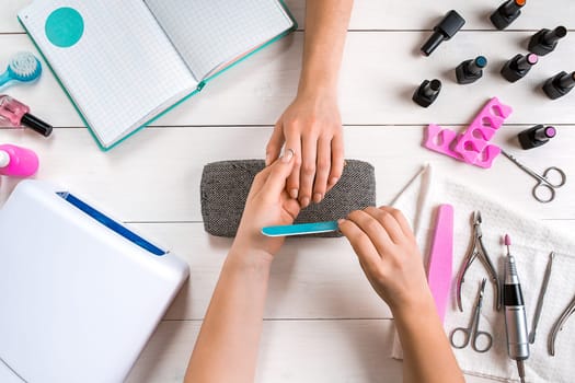 Nail care. Closeup of female hands filing nails with professional nail file in beauty nail salon. Close-up of beautician hands doing perfect manicure on woman's hands. Nail hygiene. Top view