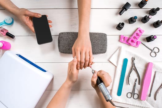 Manicure for the client. Close-up of the hands of a manicurist and client on a wooden background. Nail care. Manicure set and nail polish.