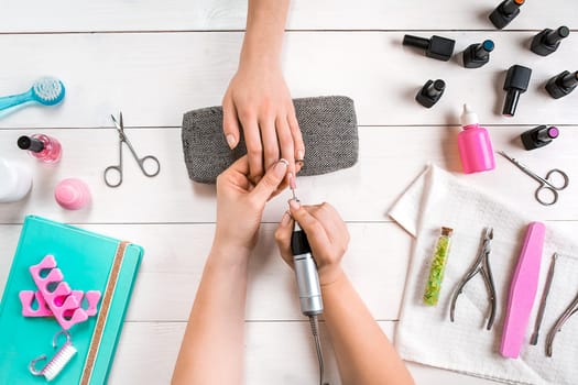 Manicure for the client. Close-up of the hands of a manicurist and client on a wooden background. Nail care. Manicure set and nail polish.