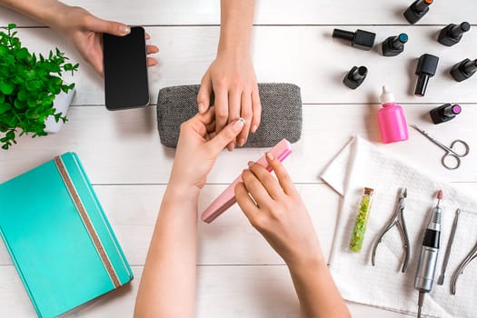 Manicure for the client. Close-up of the hands of a manicurist and client on a wooden background. Nail care. Manicure set and nail polish.
