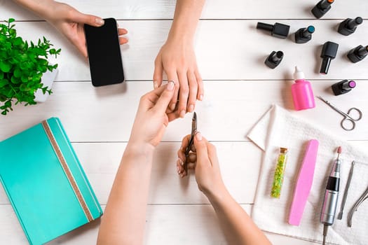 Manicure for the client. Close-up of the hands of a manicurist and client on a wooden background. Nail care. Manicure set and nail polish.