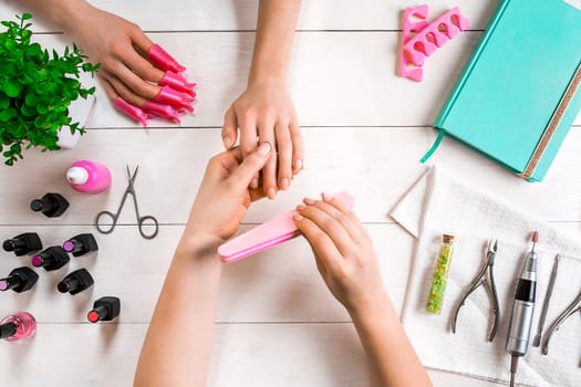 Manicure for the client. Close-up of the hands of a manicurist and client on a wooden background. Nail care. Manicure set and nail polish.