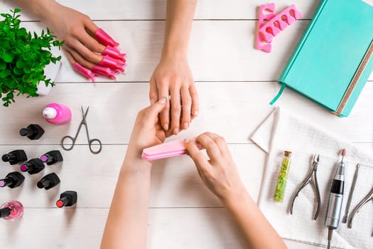 Manicure for the client. Close-up of the hands of a manicurist and client on a wooden background. Nail care. Manicure set and nail polish.