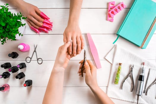 Manicure for the client. Close-up of the hands of a manicurist and client on a wooden background. Nail care. Manicure set and nail polish.
