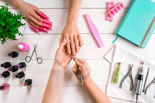Manicure for the client. Close-up of the hands of a manicurist and client on a wooden background. Nail care. Manicure set and nail polish.