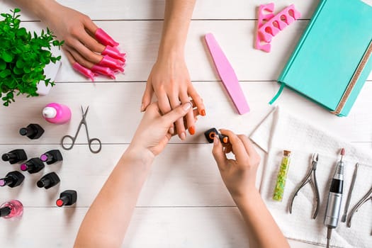 Manicure for the client. Close-up of the hands of a manicurist and client on a wooden background. Nail care. Manicure set and nail polish.