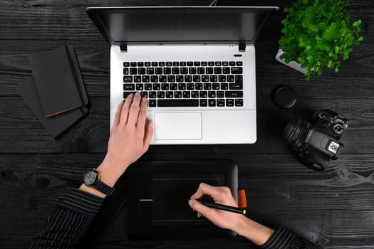 Mix of office supplies and gadgets on a wooden desk background. View from above. Female hands on the laptop keyboard