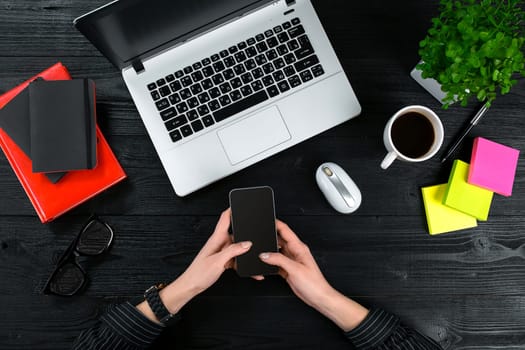 Mix of office supplies and gadgets on a wooden desk background. View from above. Female hands on the laptop keyboard