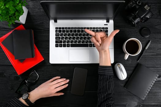 Business and technology topic: the hand of woman in a black shirt showing gesture against a black and white background laptop at the desk. Top view