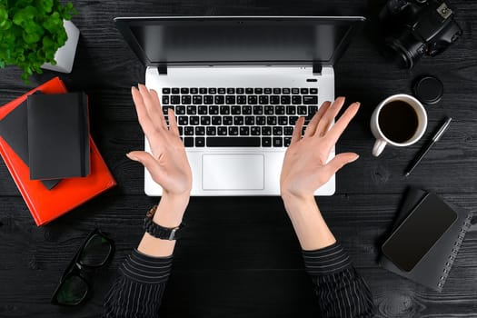 Woman working at the office table. Top view of human hands, laptop keyboard, a cup of coffee, smartphone, notebook and a flower on a wooden table background. Woman clapping her hands