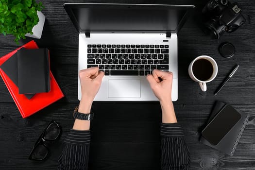 Business and technology topic: the hand of woman in a black shirt showing gesture against a black and white background laptop at the desk. Top view