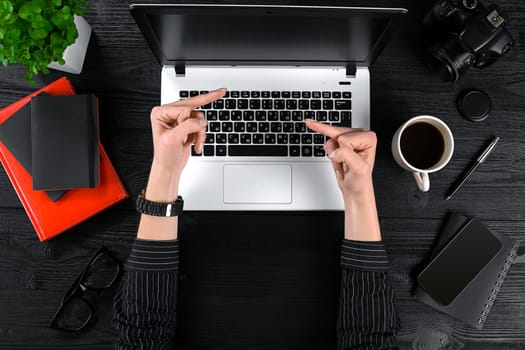 Woman working at the office table. Top view of human hands, laptop keyboard, a cup of coffee, smartphone, notebook and a flower on a wooden table background. Woman shows indecent gestures with her hands