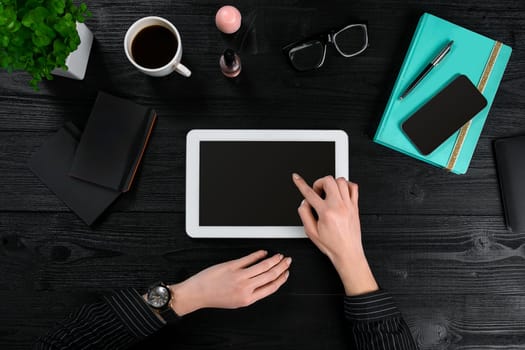Mix of office supplies and gadgets on a wooden desk background. View from above. In the female hands of a tablet