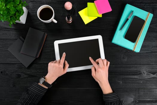 Mix of office supplies and gadgets on a wooden desk background. View from above. In the female hands of a tablet