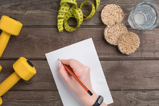 Concept diet, slimming plan with vegetables top view mock up. A female hand in a sports bracelet writes an article about proper nutrition
