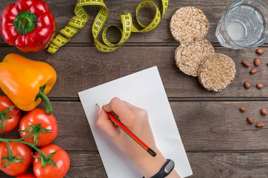 Concept diet, slimming plan with vegetables top view mock up. A female hand in a sports bracelet writes an article about proper nutrition