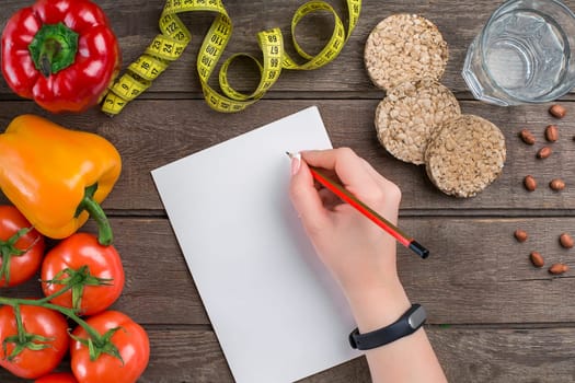 Concept diet, slimming plan with vegetables top view mock up. A female hand in a sports bracelet writes an article about proper nutrition