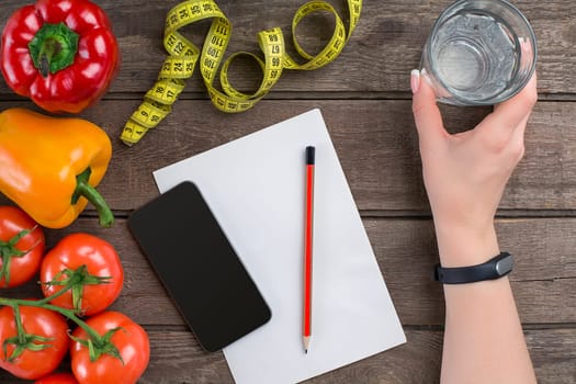 Concept diet, slimming plan with vegetables top view mock up. A female hand in a sports bracelet writes an article about proper nutrition