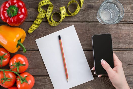 oncept diet, slimming plan with vegetables top view mock up. A female hand in a sports bracelet writes an article about proper nutrition
