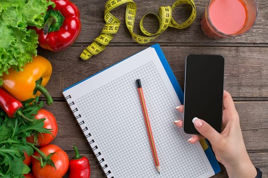 Concept diet, slimming plan with vegetables top view mock up. A female hand in a sports bracelet writes an article about proper nutrition