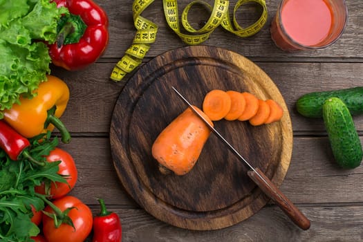 Glass of tomato juice with vegetables and measuring tape on wooden table close-up. On the cutting board is sliced carrots. Copy space. Top view