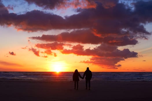 Silhouette, couple holding hands at sunset and on beach walking together. Love or care, holiday or vacation and shadows of people on the seashore for embrace for romance date or honeymoon outdoor.