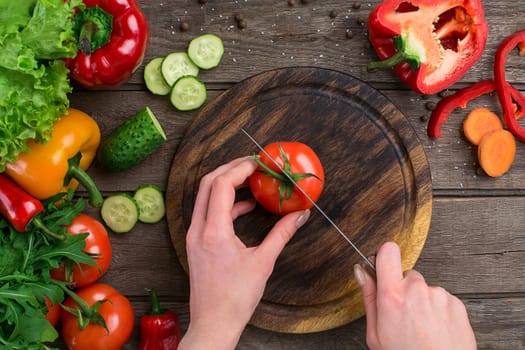 Sport and diet. Sliced Vegetables. Peppers, tomatoes, salad on rustic background. Top view. Copy space. Hands that cut a tomato on a board