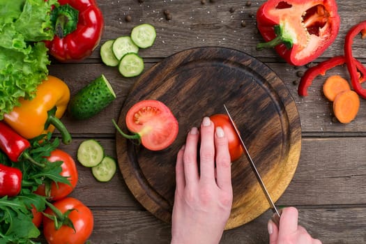 Female hands cutting tomato at table, top view. On the table vegetables and a wooden board