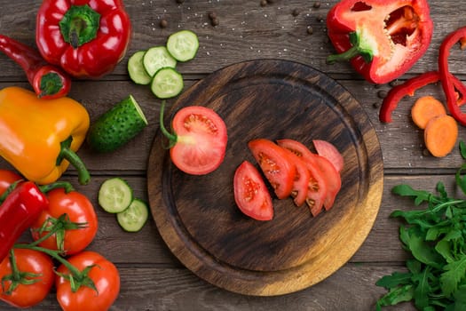 Cut tomato on a wooden board and vegetables on a table. Copy space. Top view