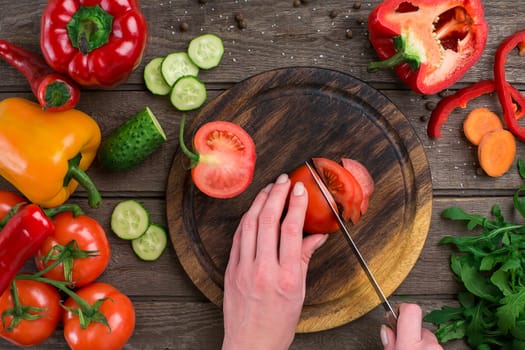 Female hands cutting tomato at table, top view. On the table vegetables and a wooden board