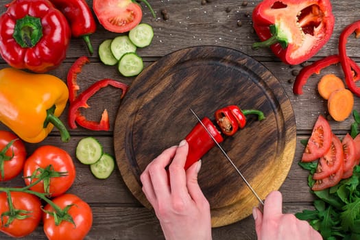 Female hands cutting hot peppers at table, top view. On the table vegetables and a wooden board