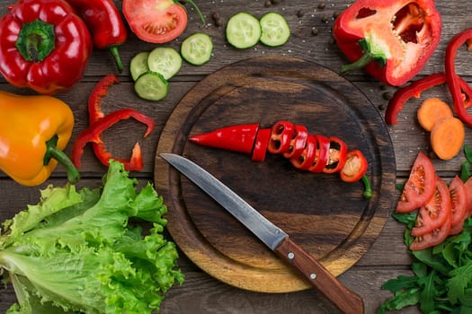 Cut pepper on a wooden board and vegetables on a table. Copy space. Top view