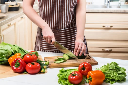 Young woman cooking in the kitchen at home. Healthy food. Diet. Dieting concept. Healthy lifestyle. Cooking at home. Prepare food. A woman cuts a cucumber and vegetables with a knife.