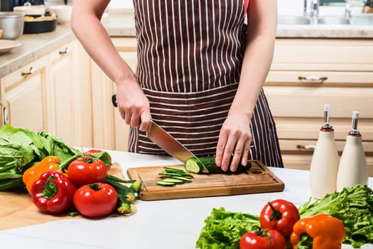 Young woman cooking in the kitchen at home. Healthy food. Diet. Dieting concept. Healthy lifestyle. Cooking at home. Prepare food. A woman cuts a cucumber and vegetables with a knife.