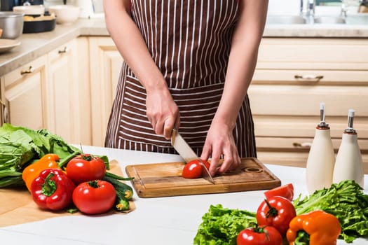 Young woman cooking in the kitchen at home. Healthy food. Diet. Dieting concept. Healthy lifestyle. Cooking at home. Prepare food. A woman cuts a tomato and vegetables with a knife.
