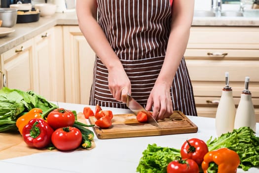 Young woman cooking in the kitchen at home. Healthy food. Diet. Dieting concept. Healthy lifestyle. Cooking at home. Prepare food. A woman cuts a tomato and vegetables with a knife.