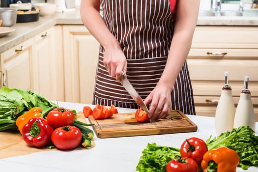 Young woman cooking in the kitchen at home. Healthy food. Diet. Dieting concept. Healthy lifestyle. Cooking at home. Prepare food. A woman cuts a tomato and vegetables with a knife.