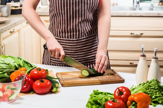 Young woman cooking in the kitchen at home. Healthy food. Diet. Dieting concept. Healthy lifestyle. Cooking at home. Prepare food. A woman cuts a cucumber and vegetables with a knife.
