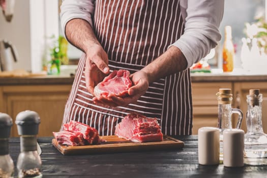 Preparation of dinner. Cooking, processing of meat. Person man's hands marinates meat - sprinkles with salt, pepper. Black wooden table, spices and herbs in the frame.