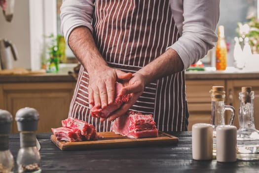 Preparation of dinner. Cooking, processing of meat beef, tenderloin . Person man's hands marinates meat - sprinkles with salt, pepper. Black wooden table, spices and herbs in the frame.