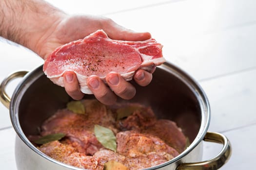 Close up of chefs hands spicing the meat. Casserole with raw meat on a white background.