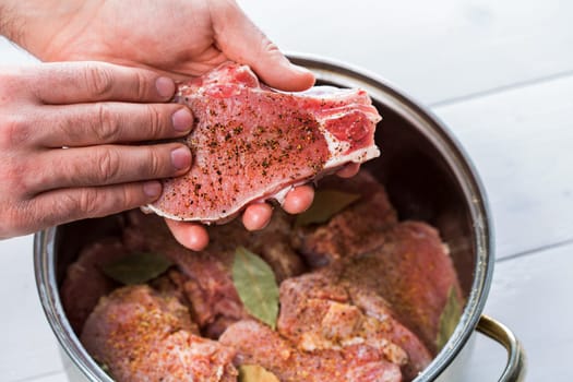 Close up of chefs hands spicing the meat. Casserole with raw meat on a white background.