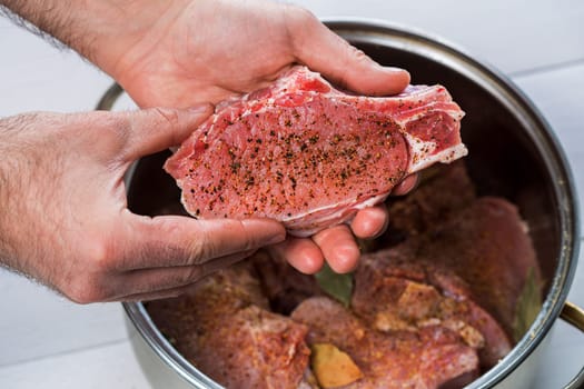 Close up of chefs hands spicing the meat. Casserole with raw meat on a white background.