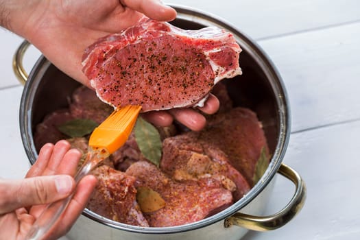 Close up of chefs hands spicing the meat. Casserole with raw meat on a white background.