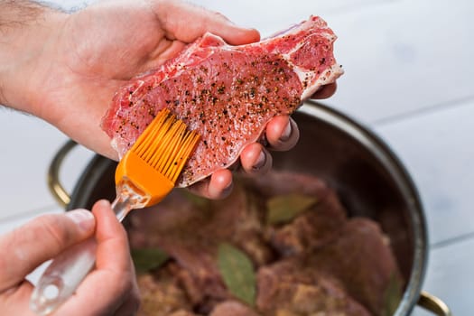 Close up of chefs hands spicing the meat. Casserole with raw meat on a white background.