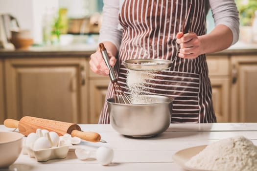 Young woman holding bowl with dough and whisk, closeup. A woman in a striped apron is cooking in the kitchen