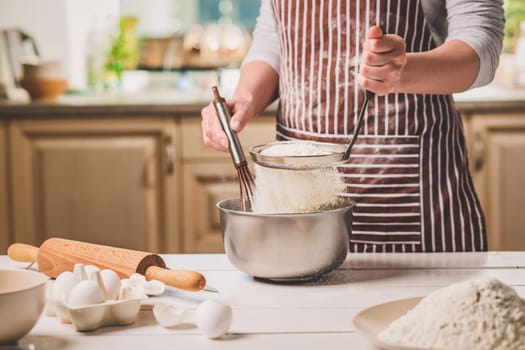 Young woman holding bowl with dough and whisk, closeup. A woman in a striped apron is cooking in the kitchen