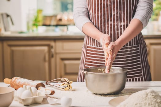 Woman hands kneading dough in iron bowl. A woman in a striped apron is cooking in the kitchen