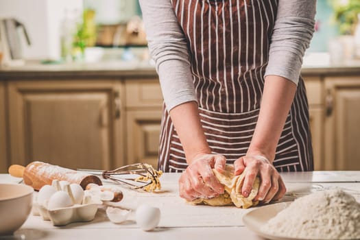 Woman hands kneading dough on kitchen table. A woman in a striped apron is cooking in the kitchen